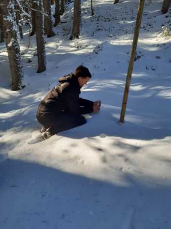 Man kneeling in the snow and collecting a sample