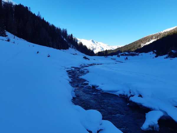 View of a valley with a river in the middle, valley is in the shade, mountain in the back is still sunlit