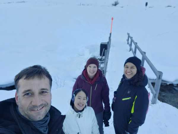 Selfie of four people in front of a small snow-covered bridge