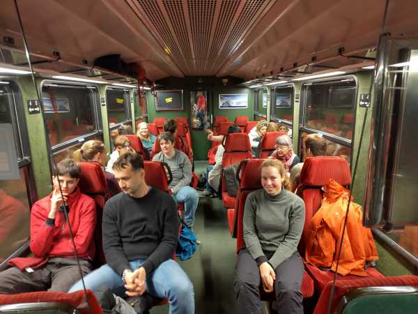 A group of people sitting in a waggon of the Jungfraubahn with red seats.
