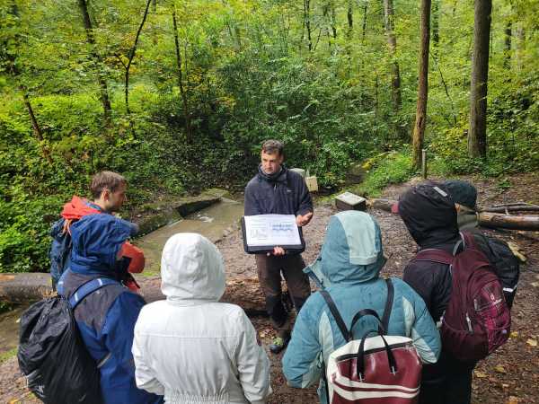 Group of people standing around man explaining something in a forest