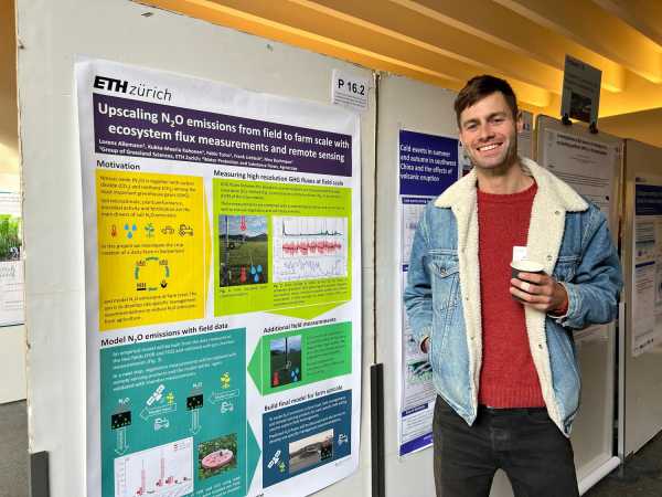 Man in front of poster with cup of cofee in hand, smiling