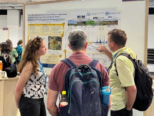 Woman explaining a poster to two men, one of them pointing at a figure on the poster