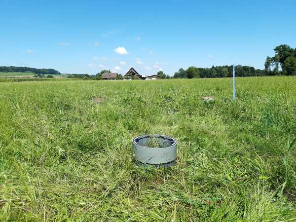 Round chamber installed in the grassland soil with a farm in the background
