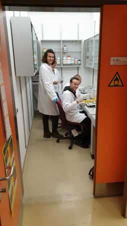 People in white lab coats in a small room, all smiling