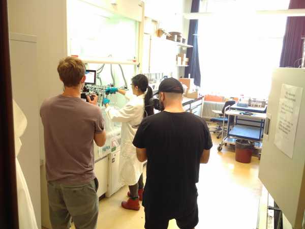 Two people filming a woman in a lab coat