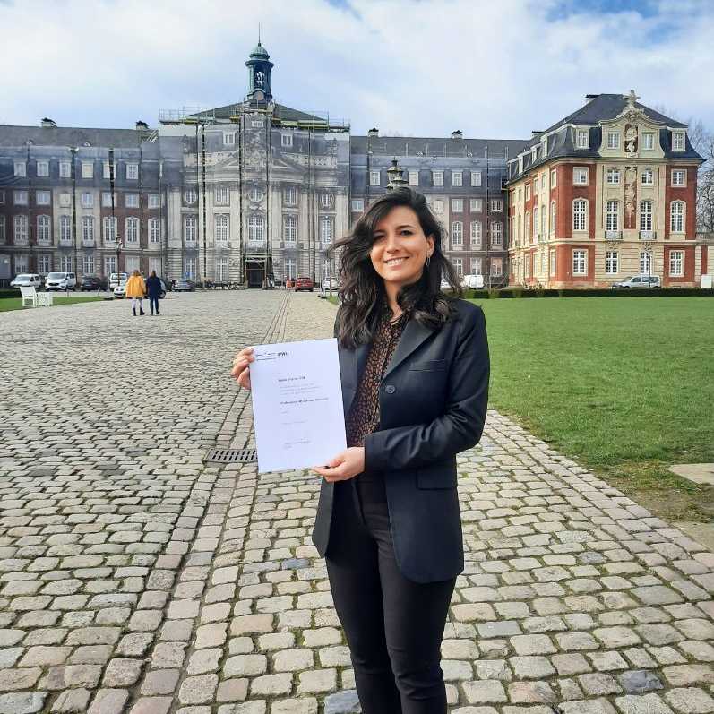 Woman showing a piece of paper in front of a nice old building