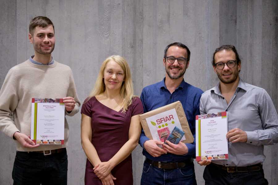Four people, three men holding an award certificate and one woman presenting the award