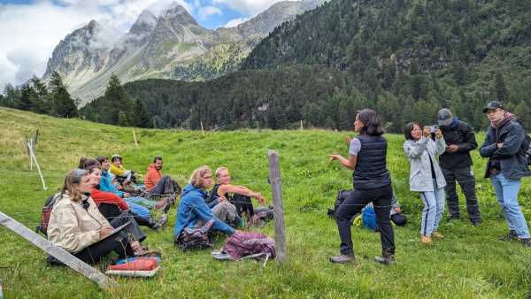 Group of people sitting on the ground listening to woman explaining something