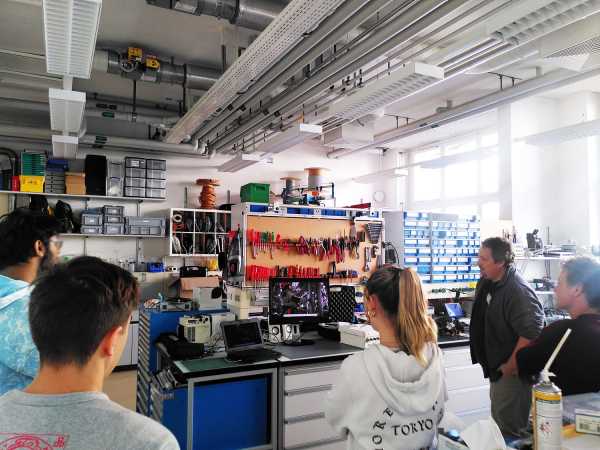 Group in workshop, man explaining something in front of wall full of tools