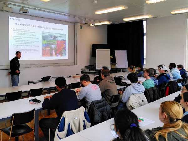 Man explaining something in a lecture hall, standing in front of screen