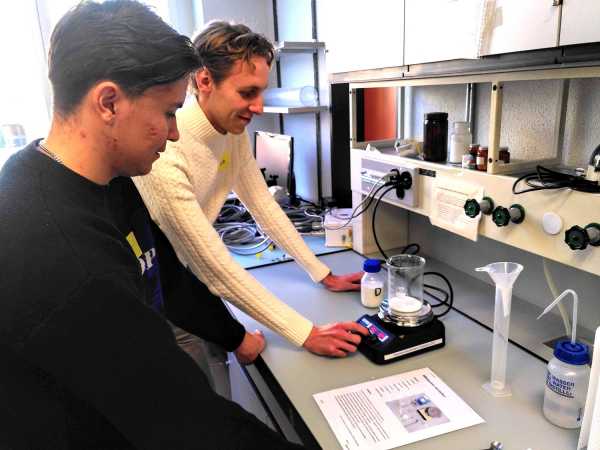 Two you men with a glass containing a white liquid on a heating plate