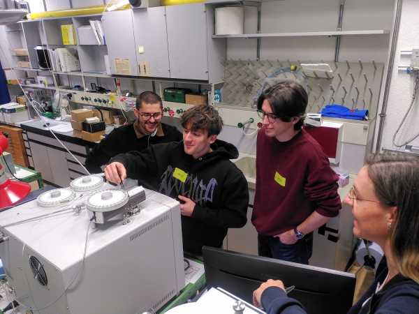 Three young men and a woman standing around a lab machine, one man putting something in an autosampler with tweezers