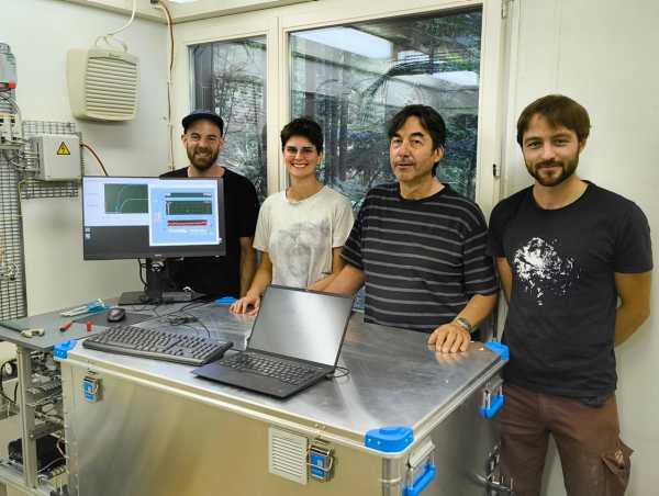 Four people standing around a box with a computer, smiling