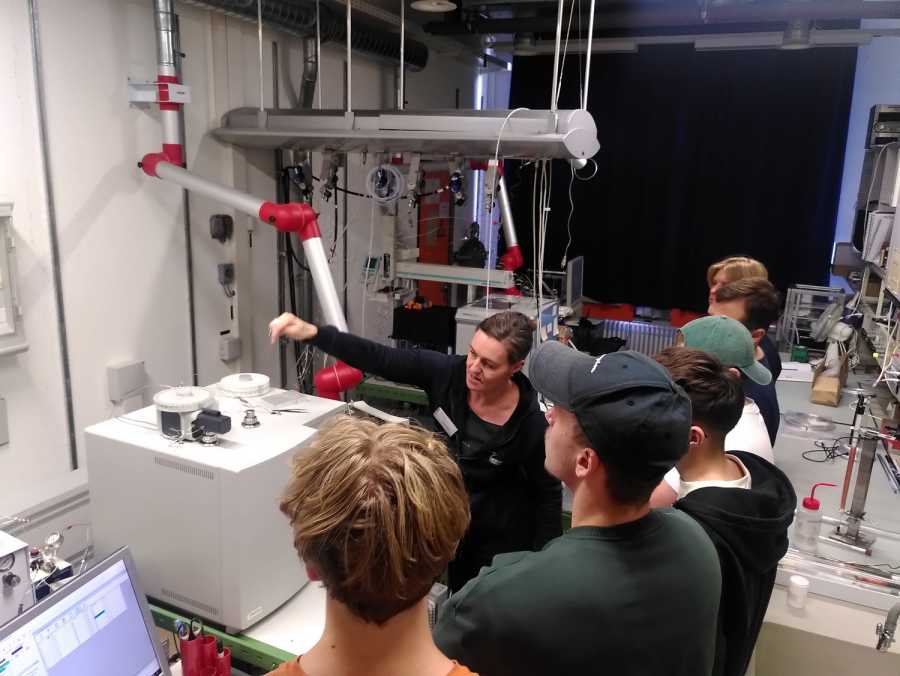 Woman explaining something in a lab pointing to an instrument, people listening